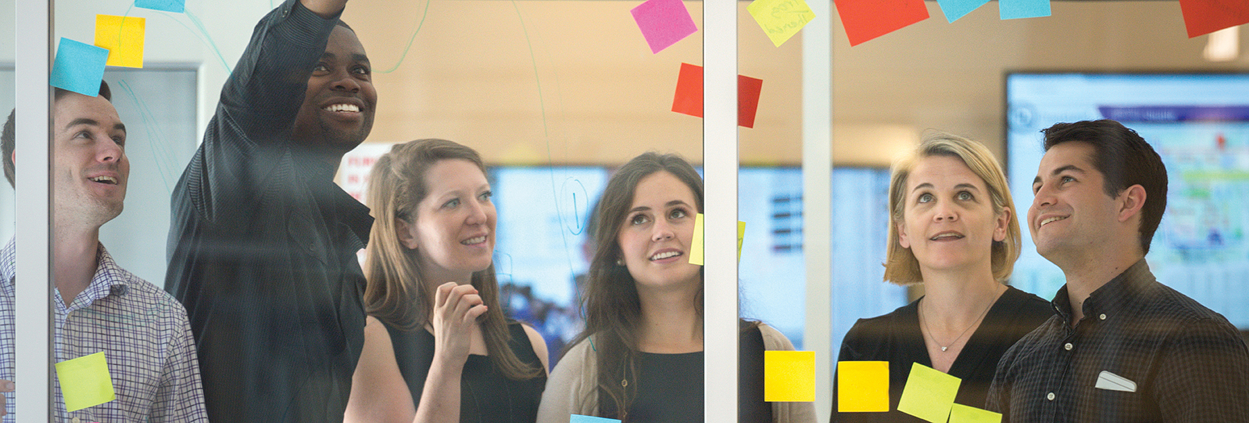 Section Image: Students and Professor Stacy Landreth Grau look at Post-it notes on a glass wall. 