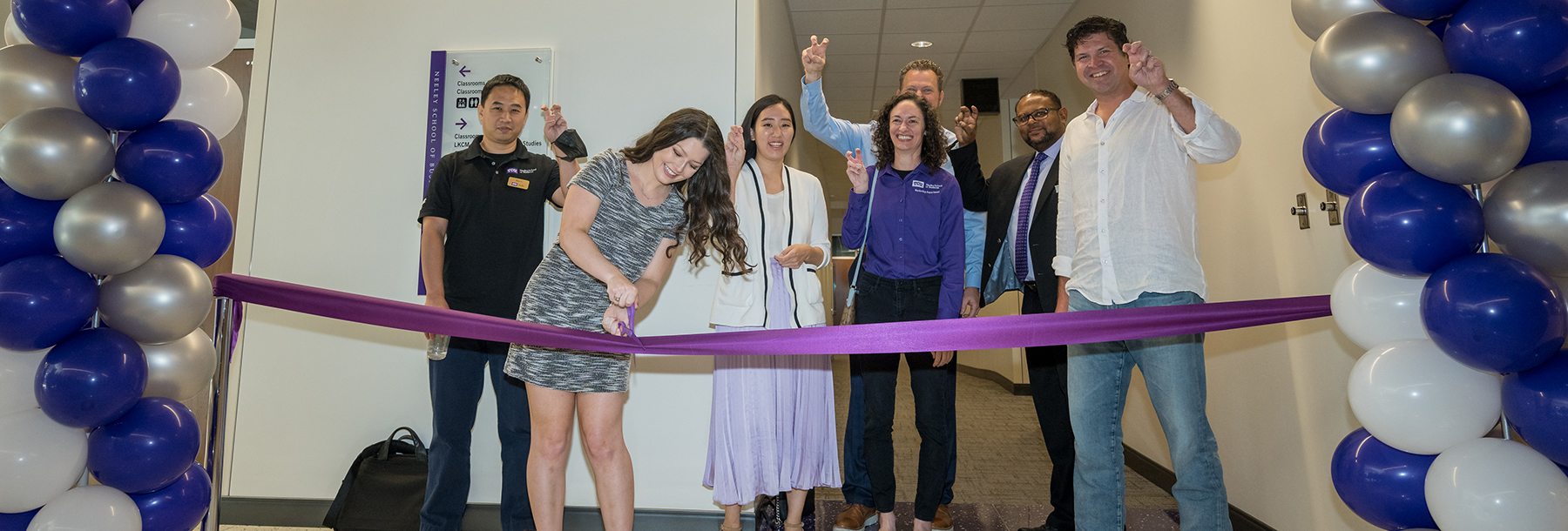 Section Image: Woman with purple scissors cuts a purple ribbon while Marketing professors with their "frogs up" outside of the Behavorial Research Lab. 
