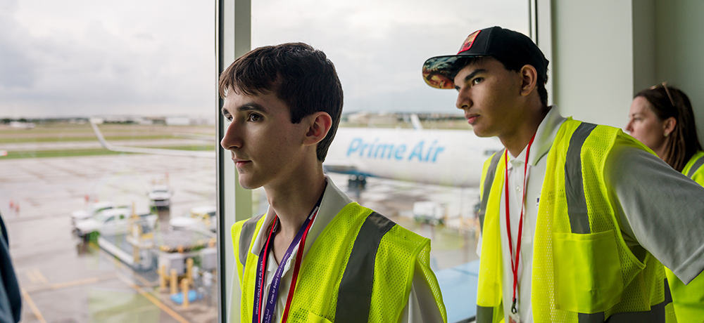 Two students looking through a window at airplanes