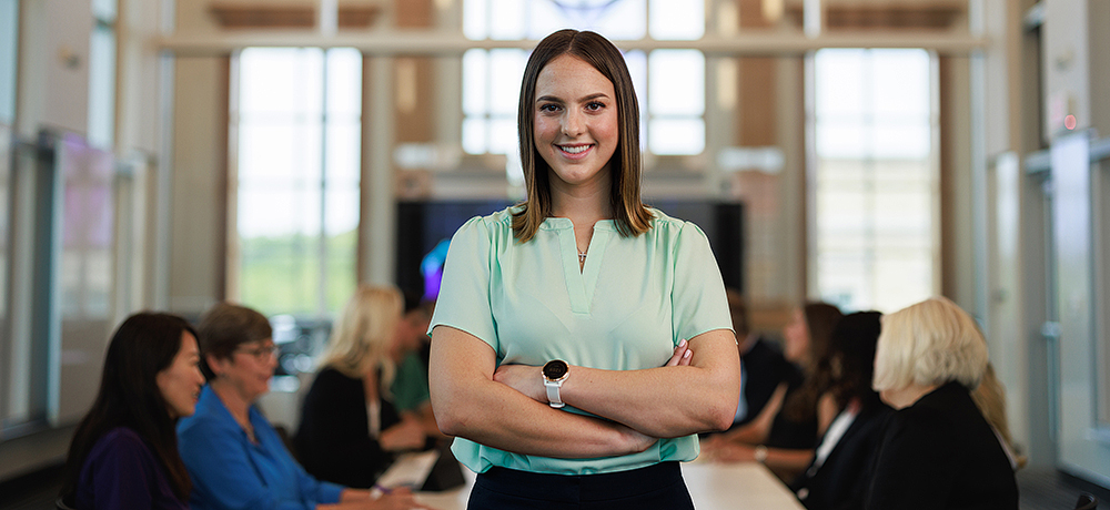 Girl with arms crossed with people at a table behind her