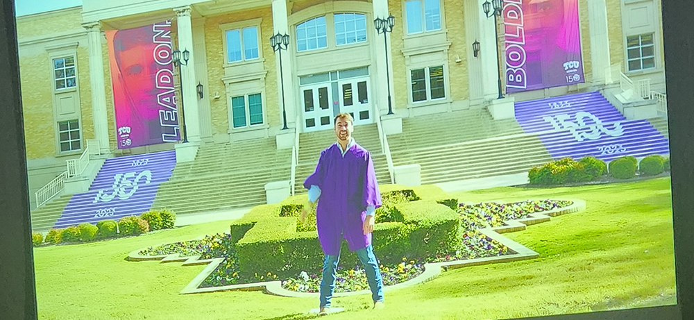 John Freeny outside the TCU library with 150th on stairs and Lead On banners wearing graduation gown