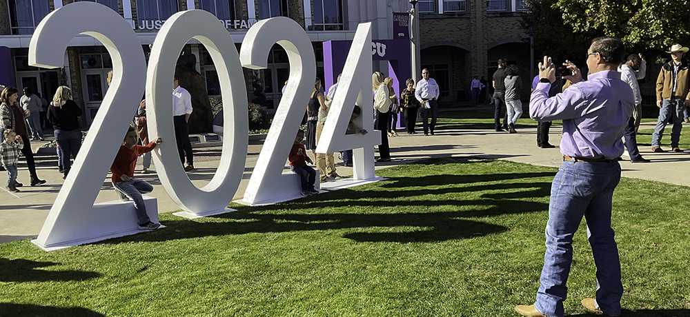 Section Image: Man taking picture of kids sitting on a huge 2024 in the lawn outside Schollmaier Arena 